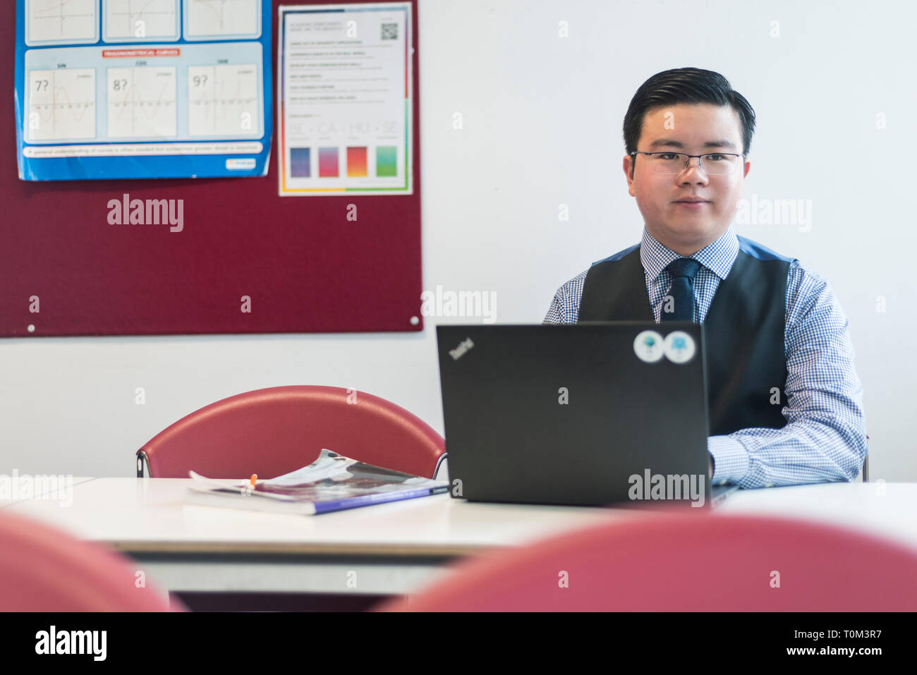 An international asian young male student sits in a classroom at a desk ...