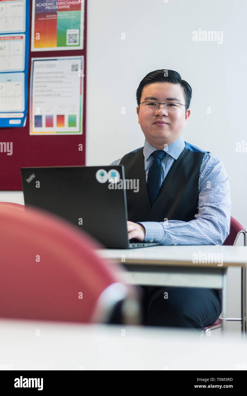 An international asian young male student sits in a classroom at a desk working and studying on his laptop in a modern classroom. Stock Photo