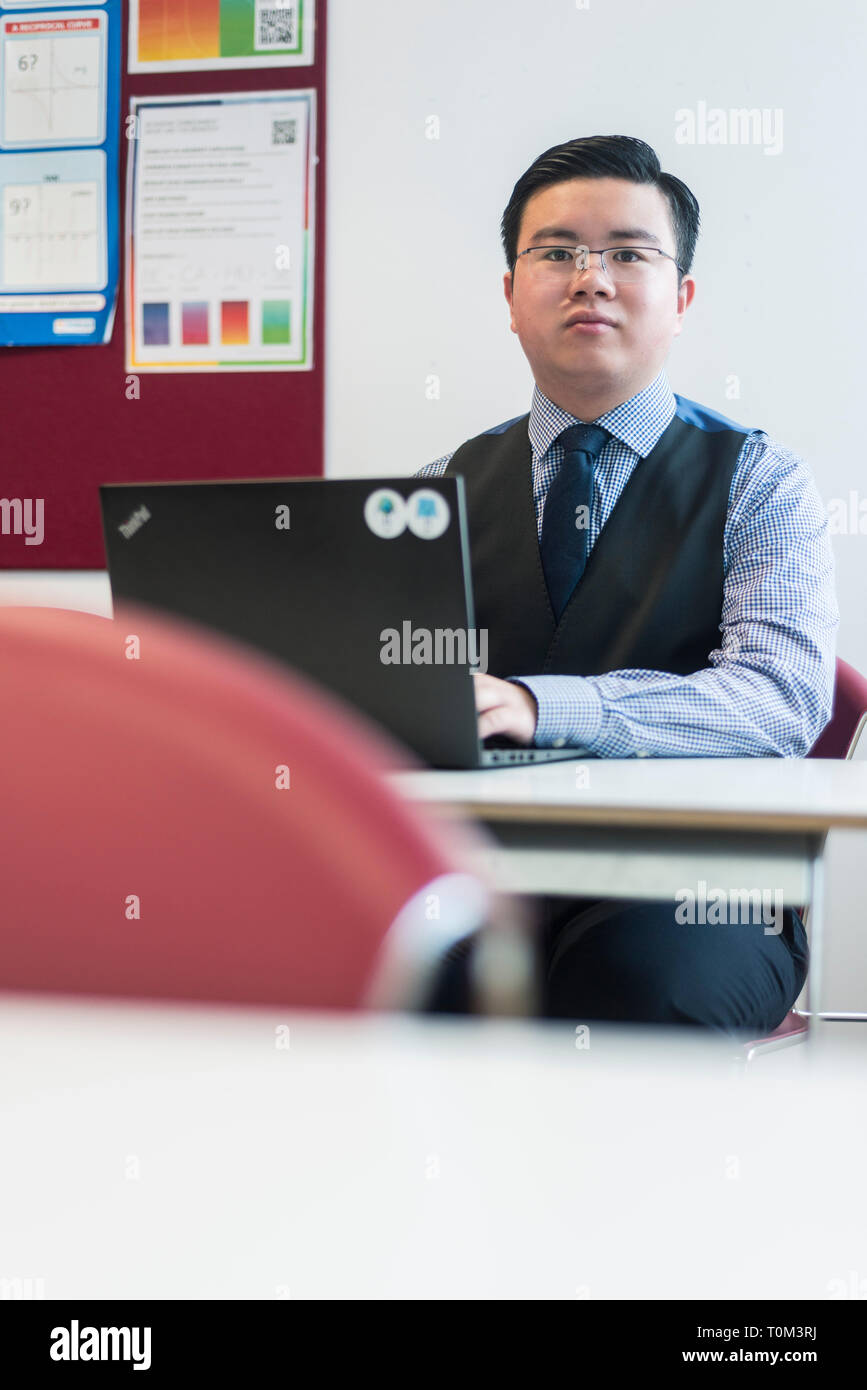 An international asian young male student sits in a classroom at a desk ...