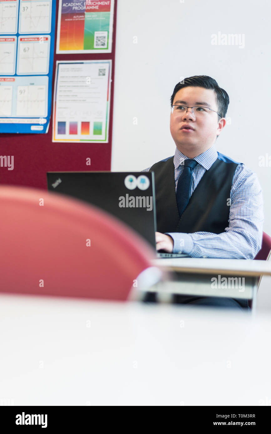 An international asian young male student sits in a classroom at a desk ...