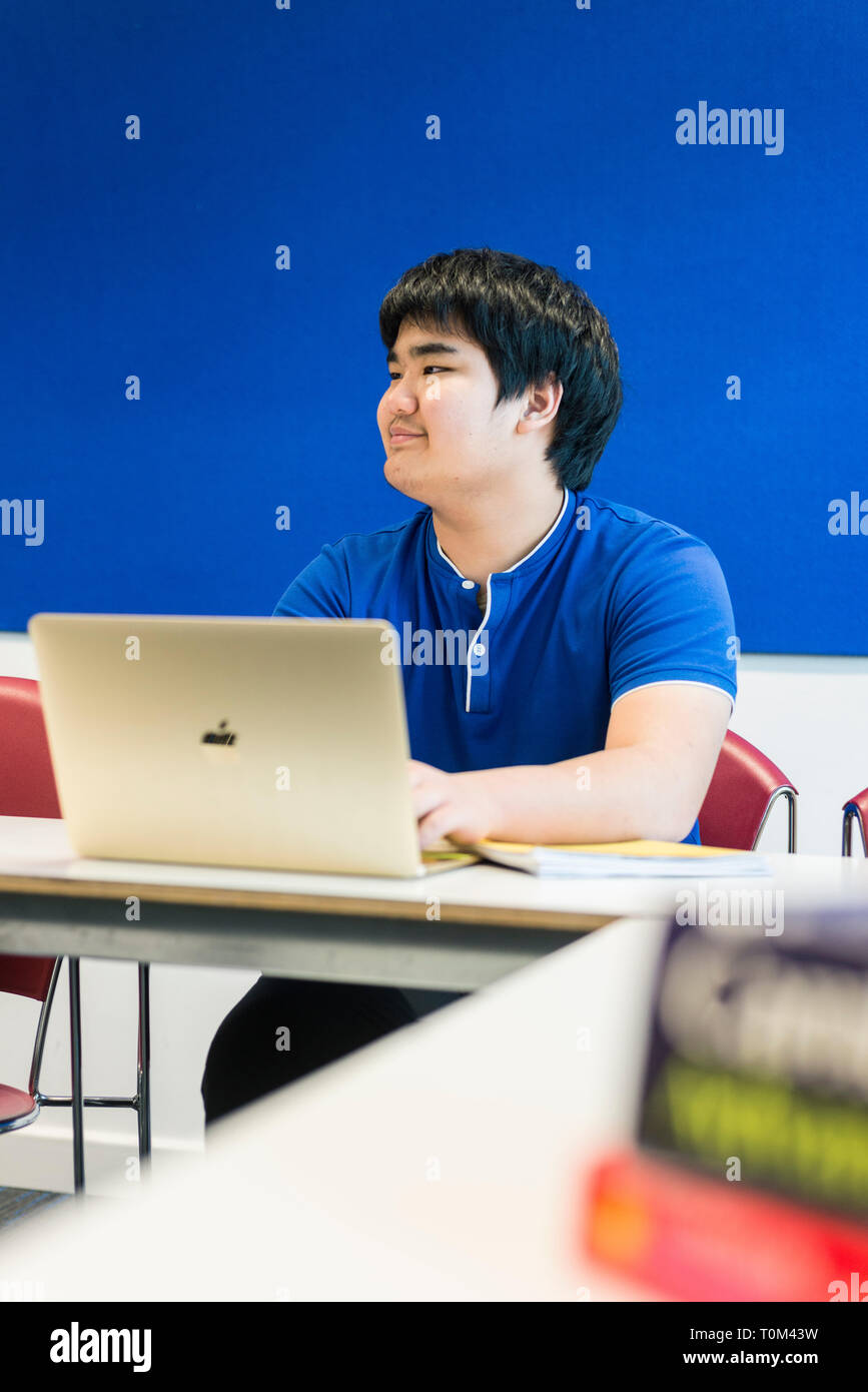 An international asian young male student sits in a classroom at a desk ...
