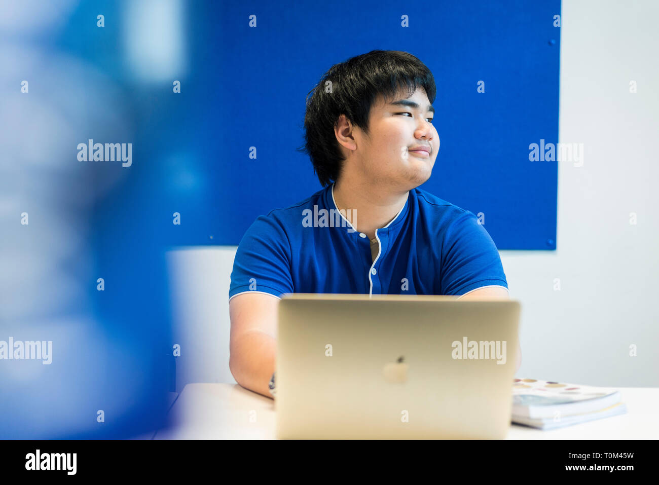 An international asian young male student sits in a classroom at a desk ...