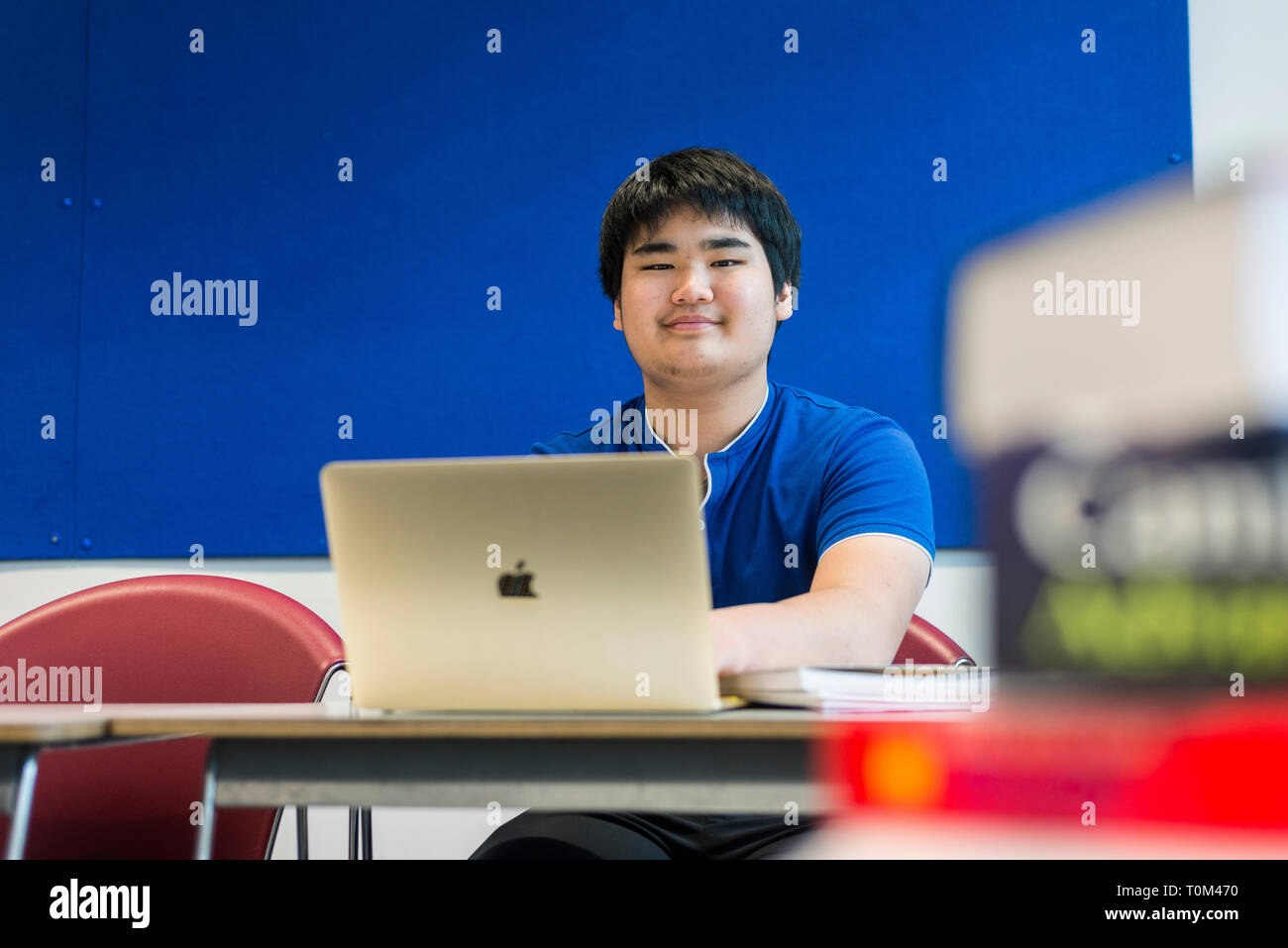 An international asian young male student sits in a classroom at a desk working and studying on his laptop in a modern classroom. Stock Photo
