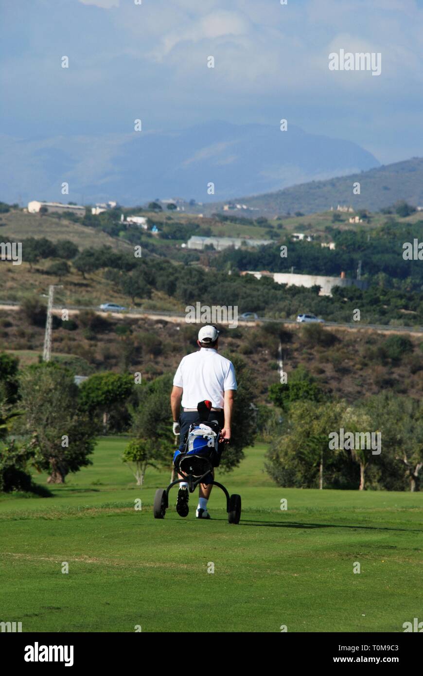 Golfer walking along with his buggy at Los Llanos de Baviera Golf, Caleta de Velez, Malaga Province, Andalusia, Spain, Western Europe. Stock Photo