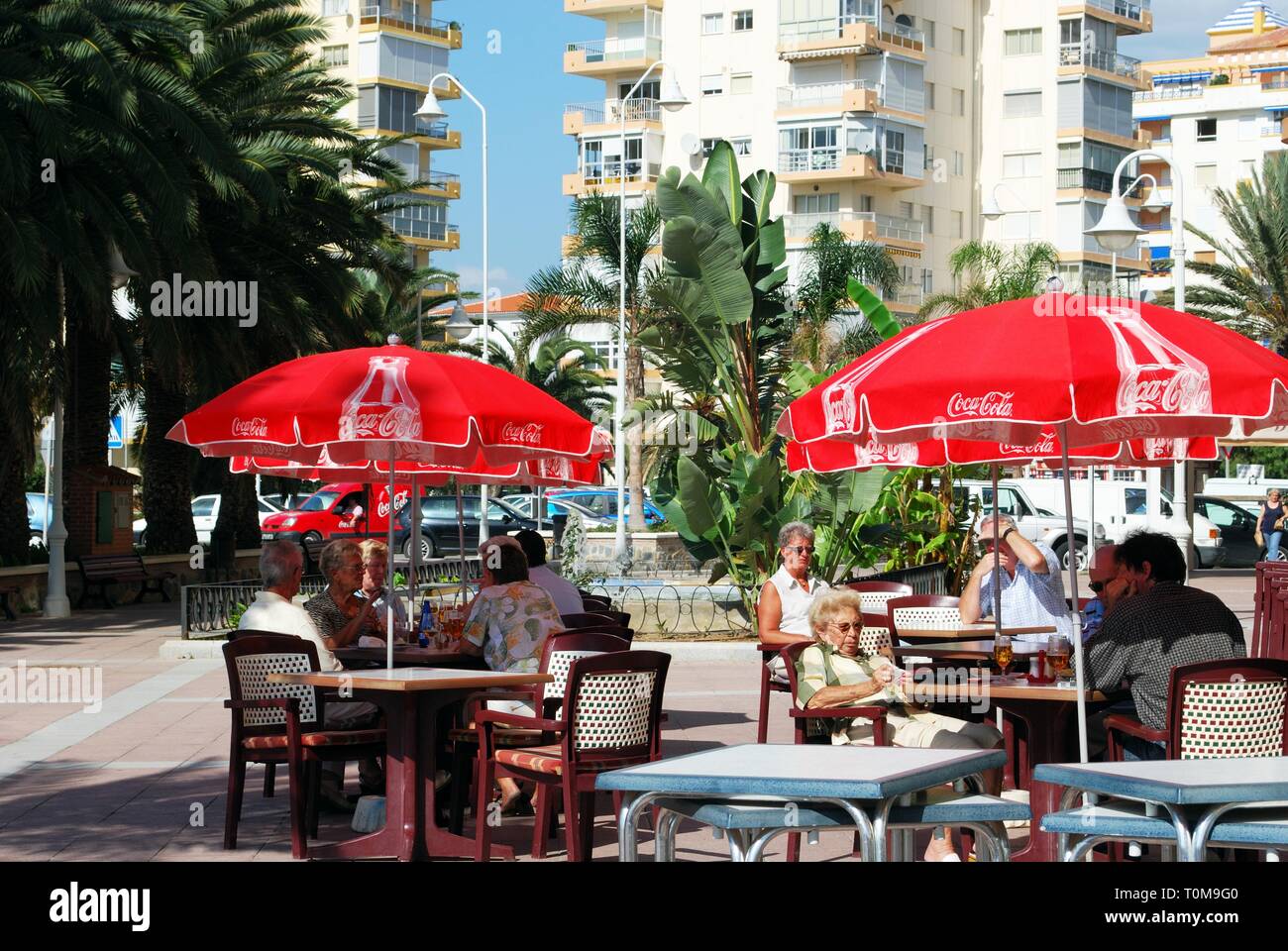 Tourists relaxing at a pavement cafe with red parasols, Lagos, Malaga Province, Andalusia, Spain, Western Europe. Stock Photo