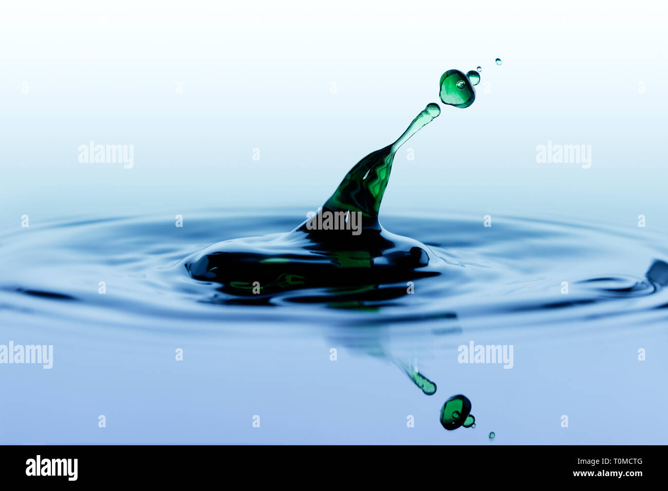Splash. Green drop falling on smooth surface of water. Stock Photo
