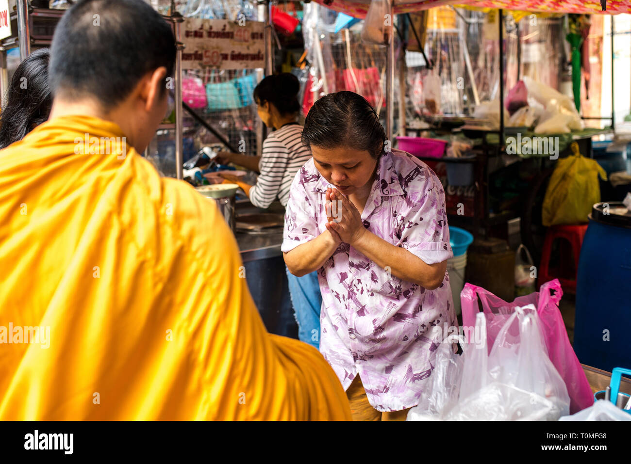 Woman in prayer position in front of a monk, market in Chinatown, Bangkok,Thailand Stock Photo