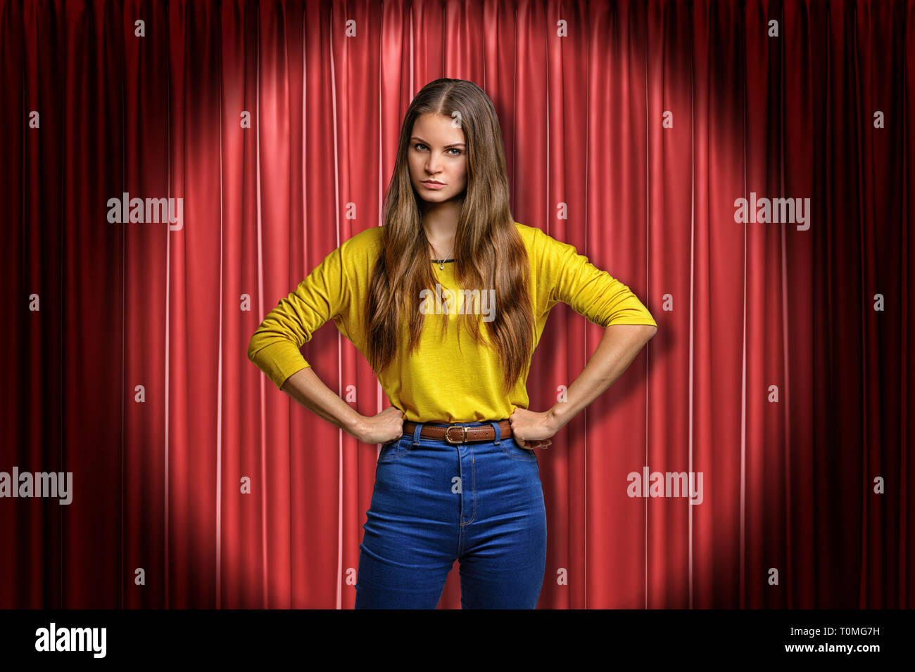 Young angry woman wearing jeans and yellow shirt on red stage curtains background Stock Photo