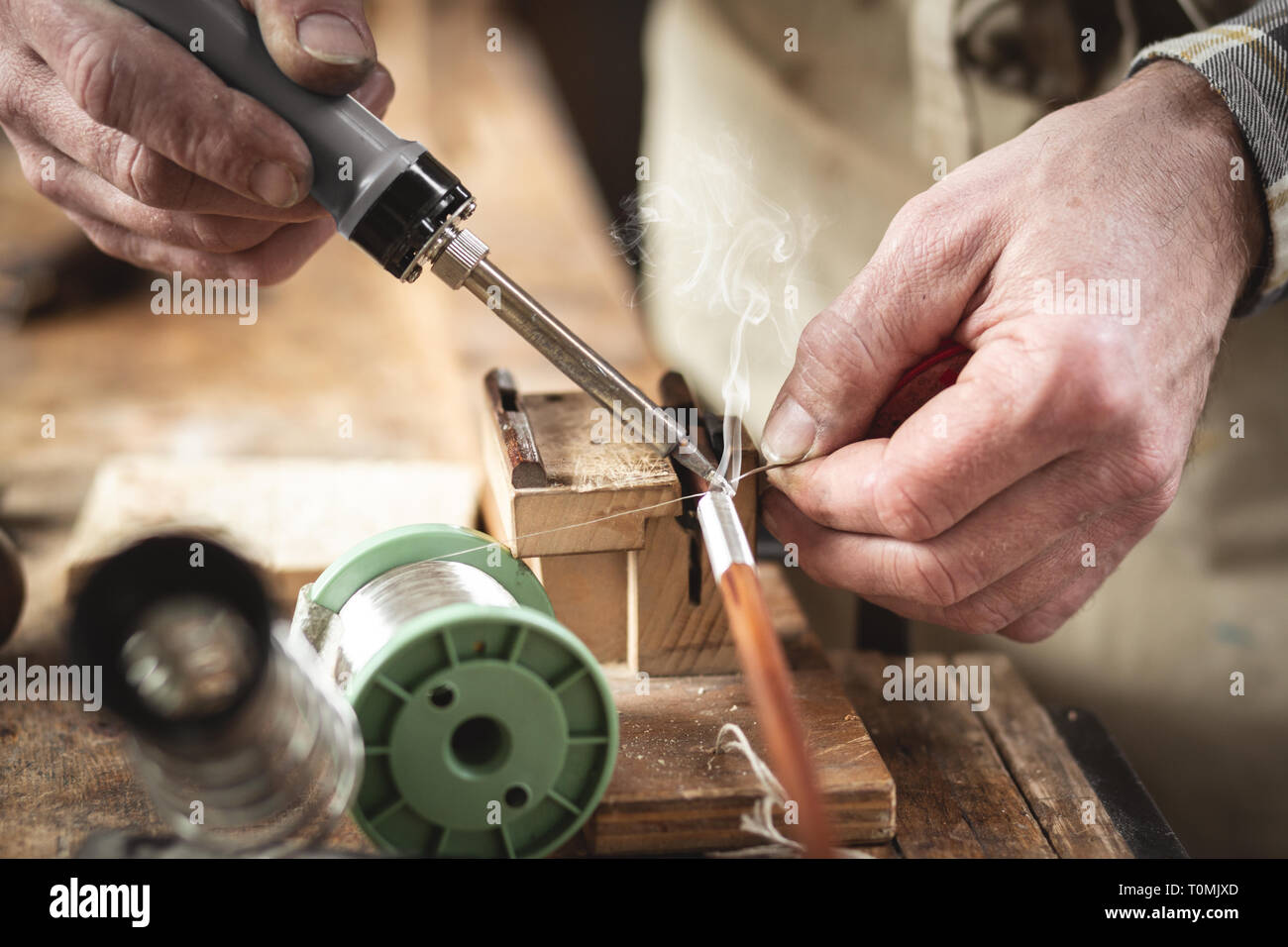 Closeup of hands using a soldering iron on a rustic workbench Stock Photo