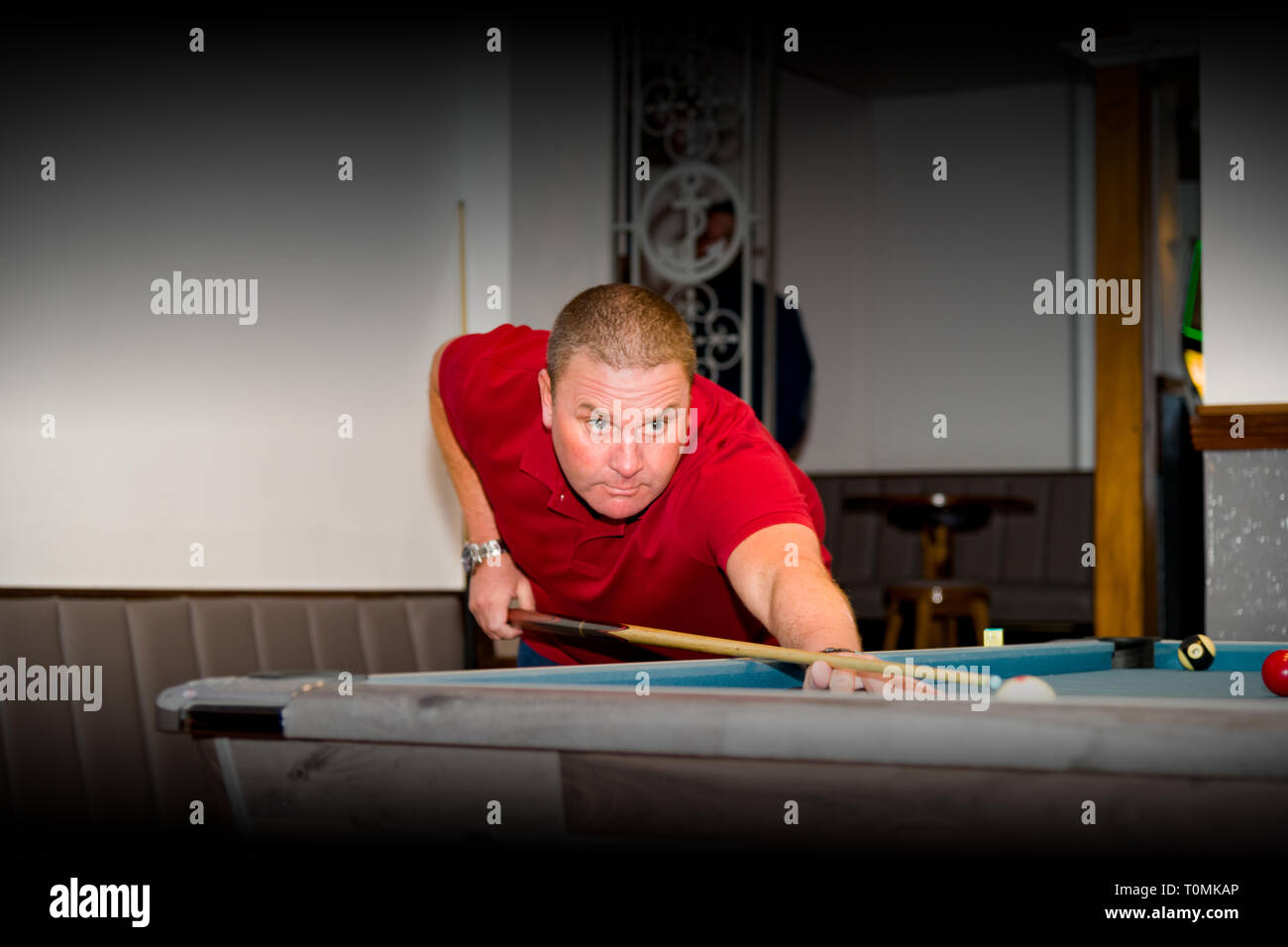 A middle aged pool player in a red shirts takes a shot Stock Photo