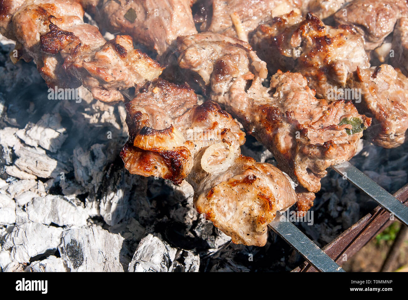 Grilled kebab cooking on metal skewer. Shashlik made of cubes of meat on the skewers during of cooking on the mangal over charcoal outdoors. Grill on  Stock Photo