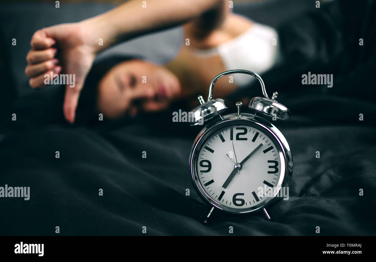 Shocked young woman waking up with alarm. Girl overslept in bed and looking alarm clock in shock