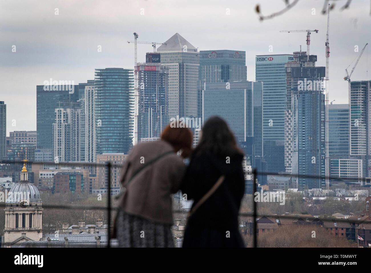 Visitors in Greenwich Park, south London, look at the view across the River Thames towards Canary Wharf. Stock Photo
