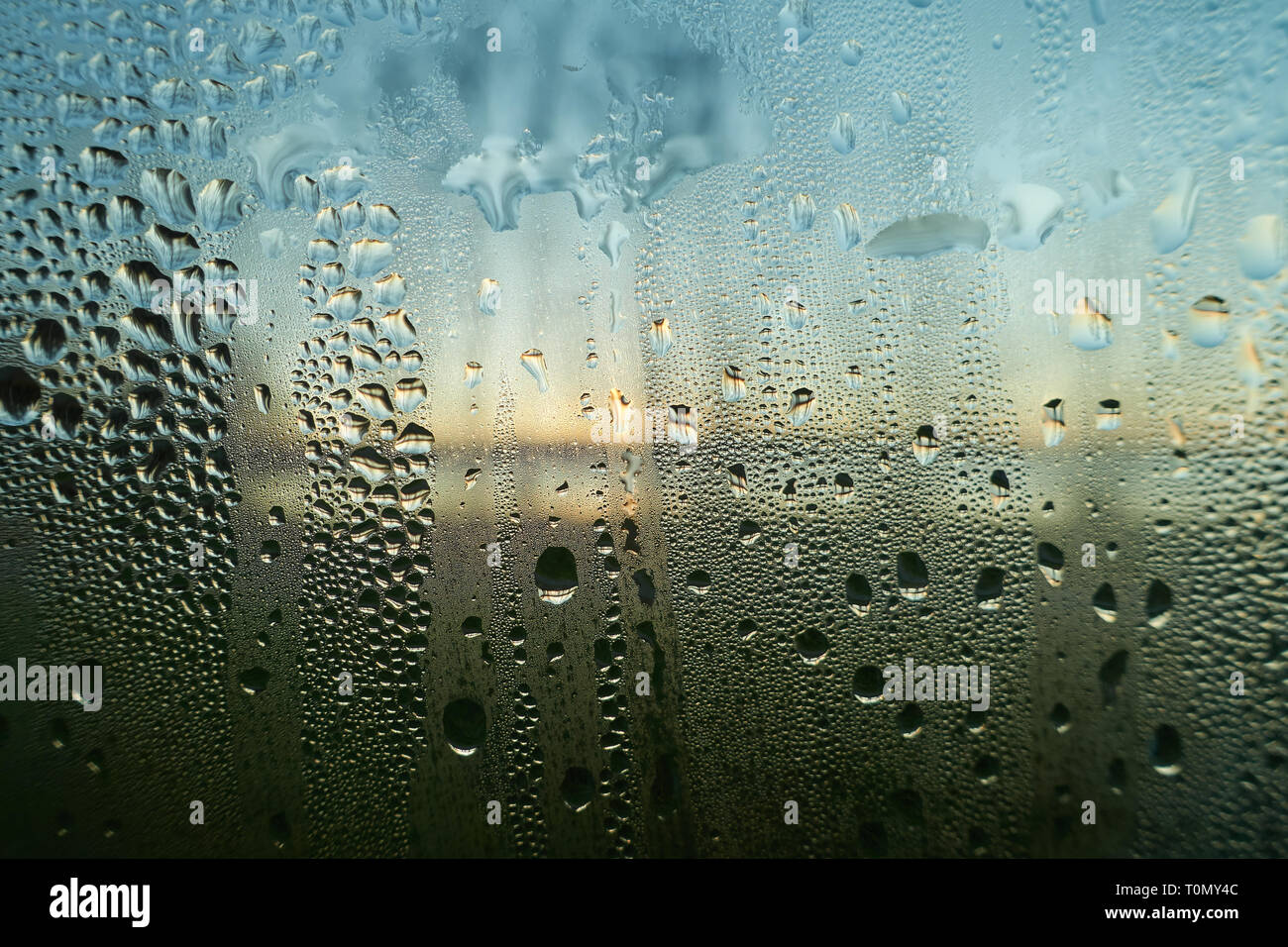 Raining water drops on a wet window closeup image. Condensed moisture on a glass surface in the morning. Sunrise on the background. Hope, faith and a  Stock Photo