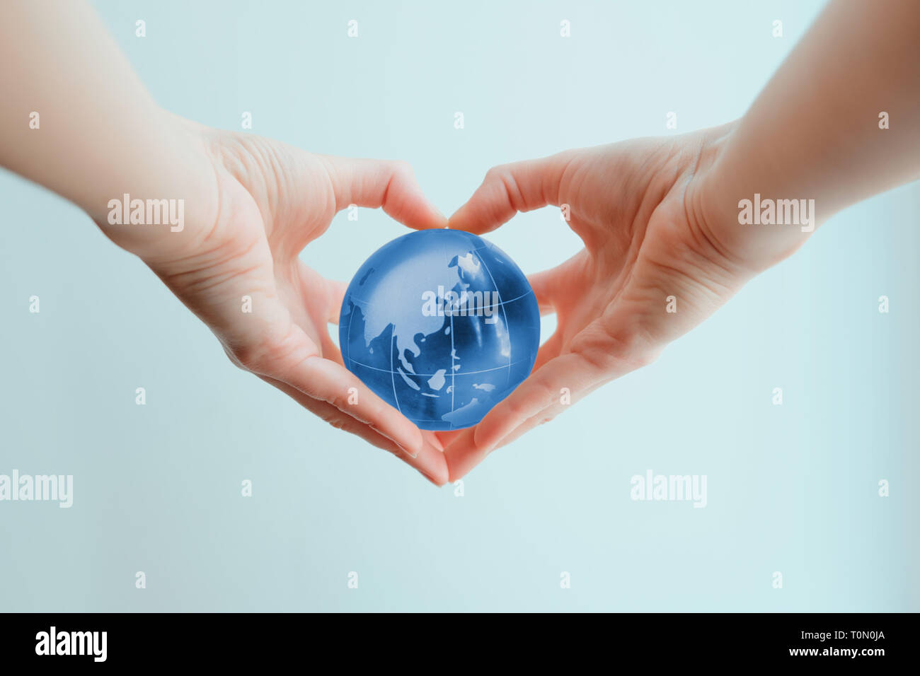 Two hands in shape of a heart holding a blue glass globe of Indoneasia and Phillipine sea Stock Photo