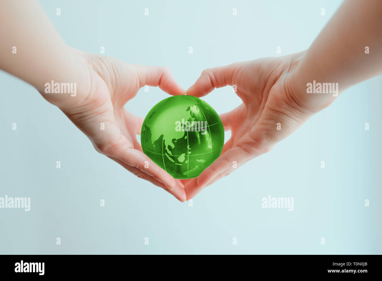 Two hands in shape of a heart holding a green glass globe of Indoneasia and Phillipine sea Stock Photo