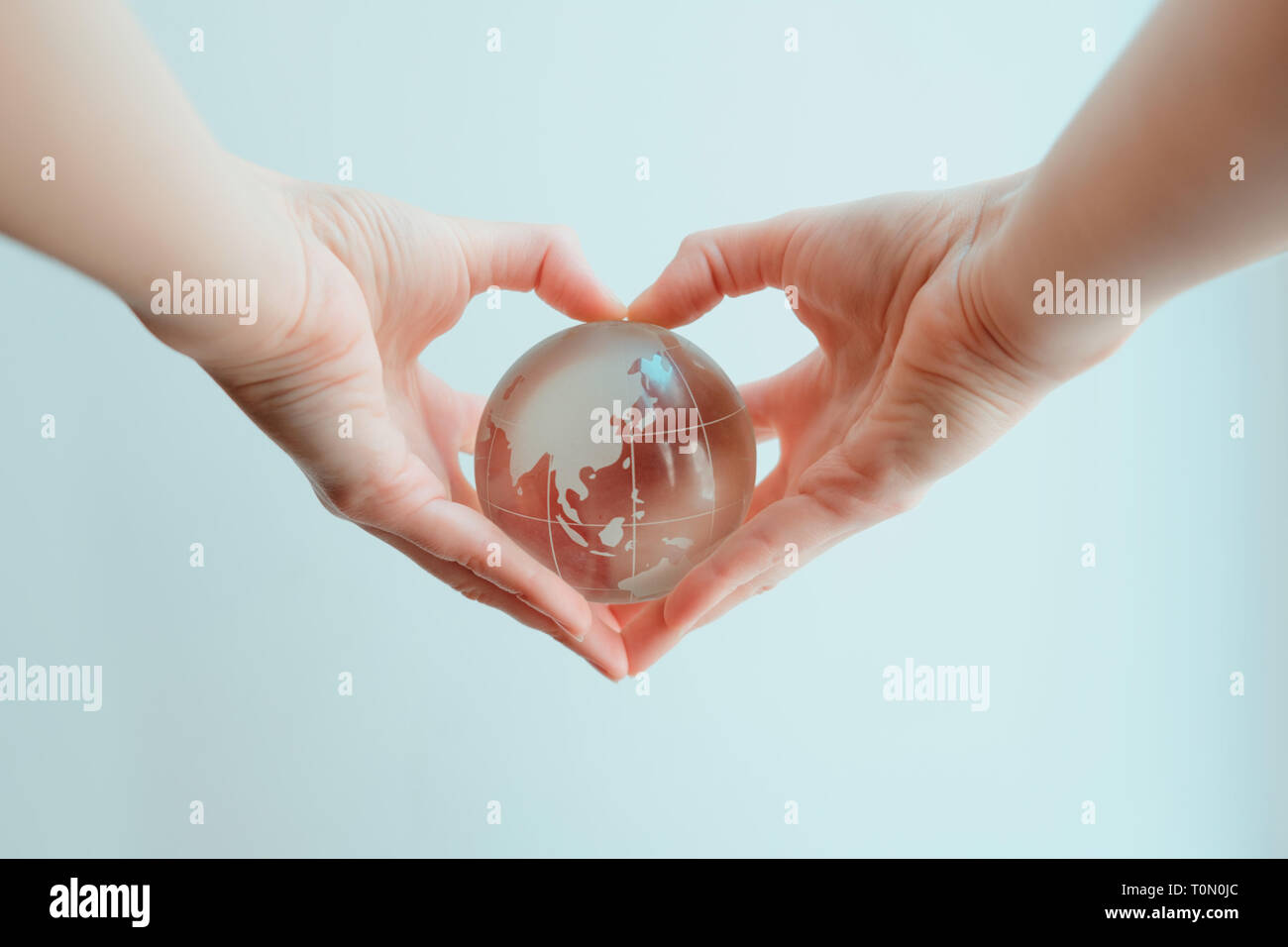 Two hands in shape of a heart holding a glass globe of Indoneasia and Phillipine sea Stock Photo