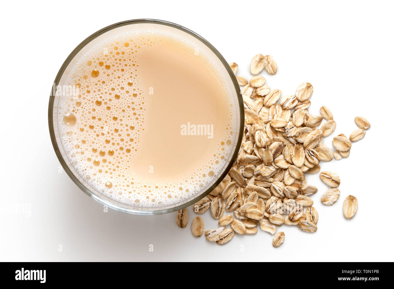 Glass of oat drink  next to a pile of dry oats isolated on white from above. Stock Photo