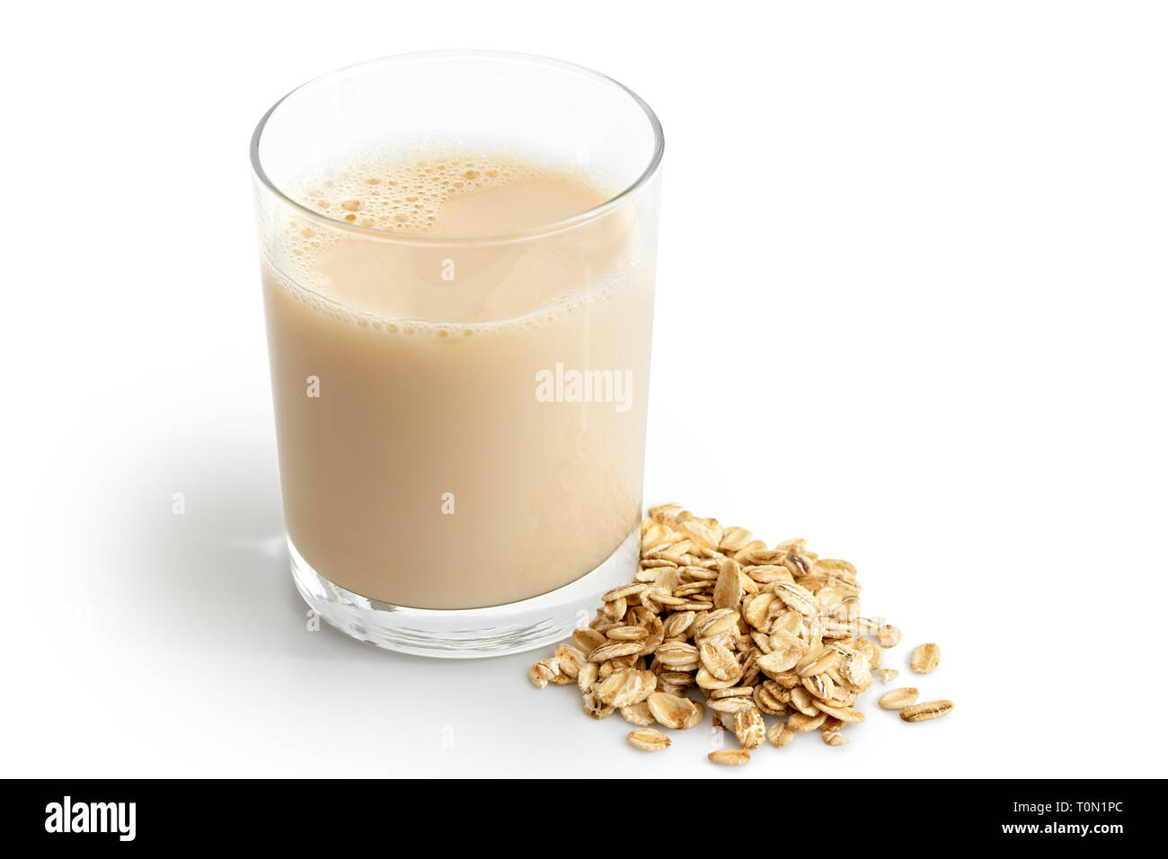 Glass of oat drink  next to a pile of dry oats isolated on white. Stock Photo