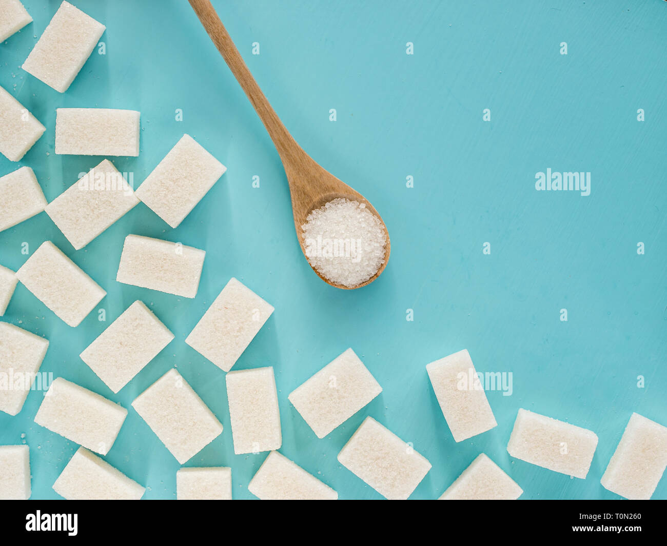 background of sugar cubes and sugar in spoon. White sugar on blue background. Sugar with copy space. Top view or flat lay Stock Photo