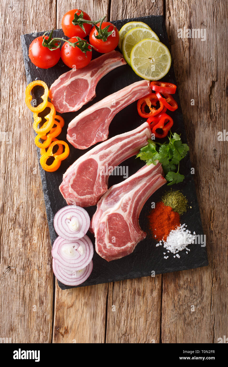 Raw lamb cutlets with fresh vegetables and spices close-up on a slate ...