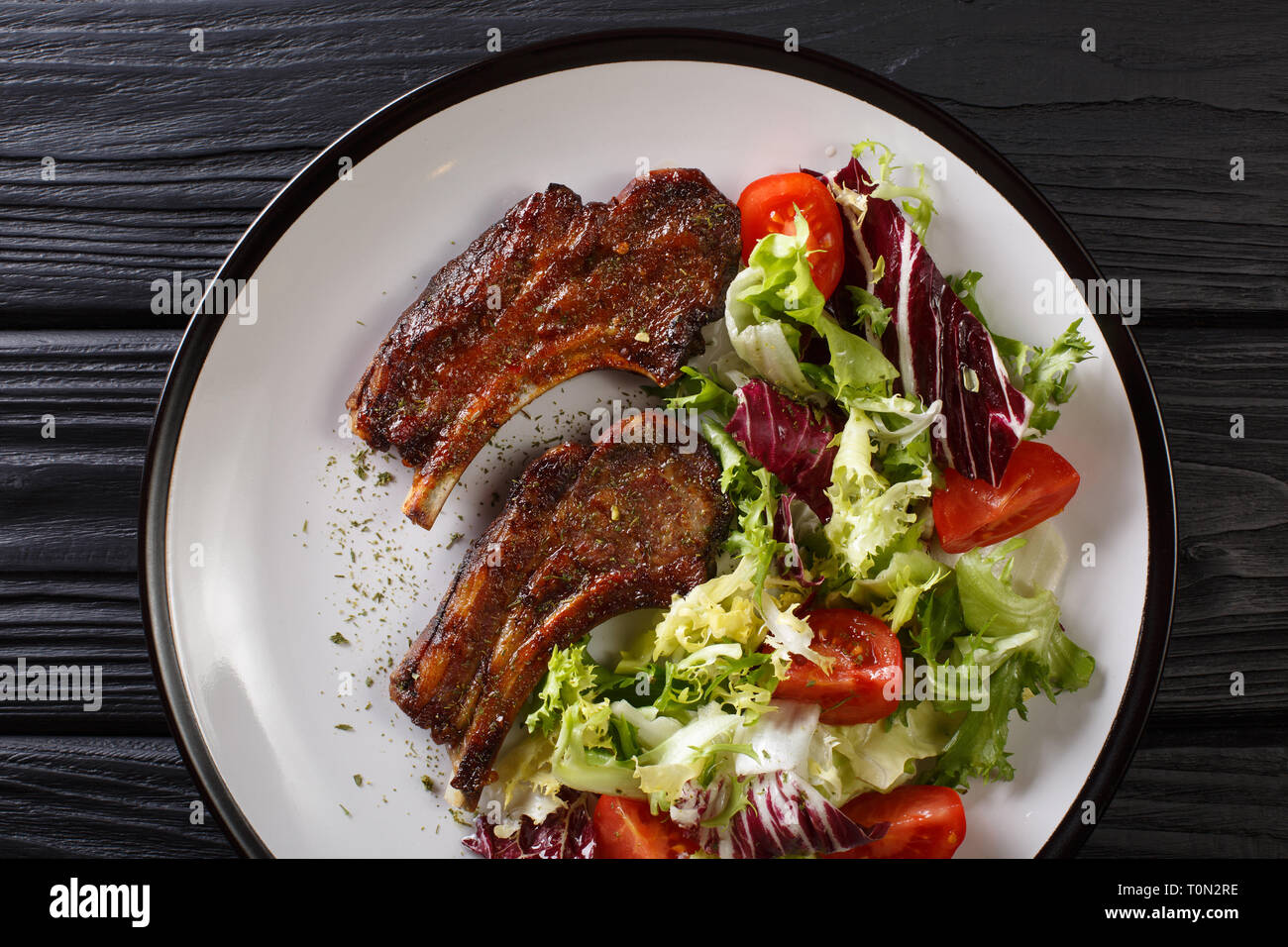 Serving fried lamb ribs with fresh vegetable salad close-up on a plate on the table. Horizontal top view from above Stock Photo