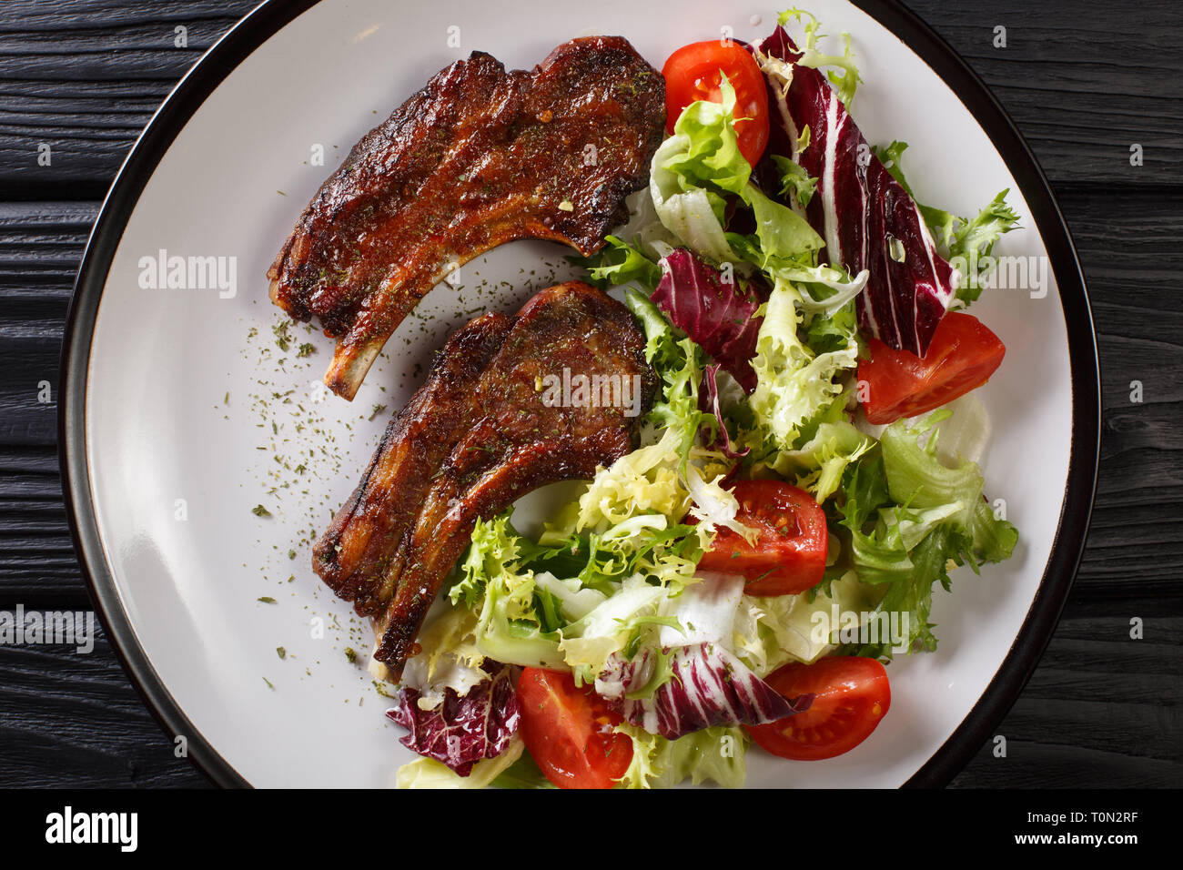 Baked lamb steak with honey served with fresh vegetable salad close-up on a plate on the table. Horizontal top view from above Stock Photo