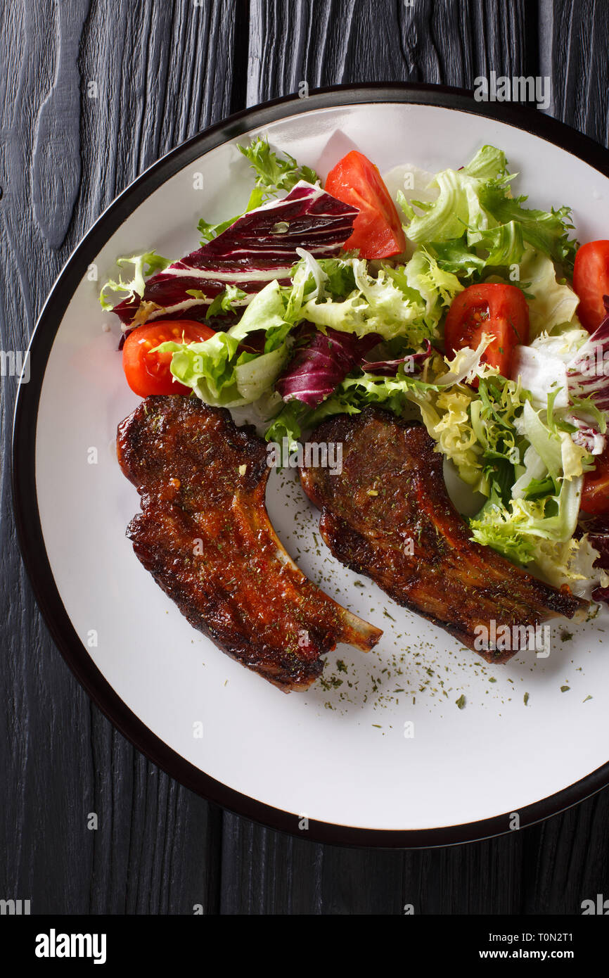 Baked lamb steak with honey served with fresh vegetable salad close-up on a plate on the table. Vertical top view from above Stock Photo