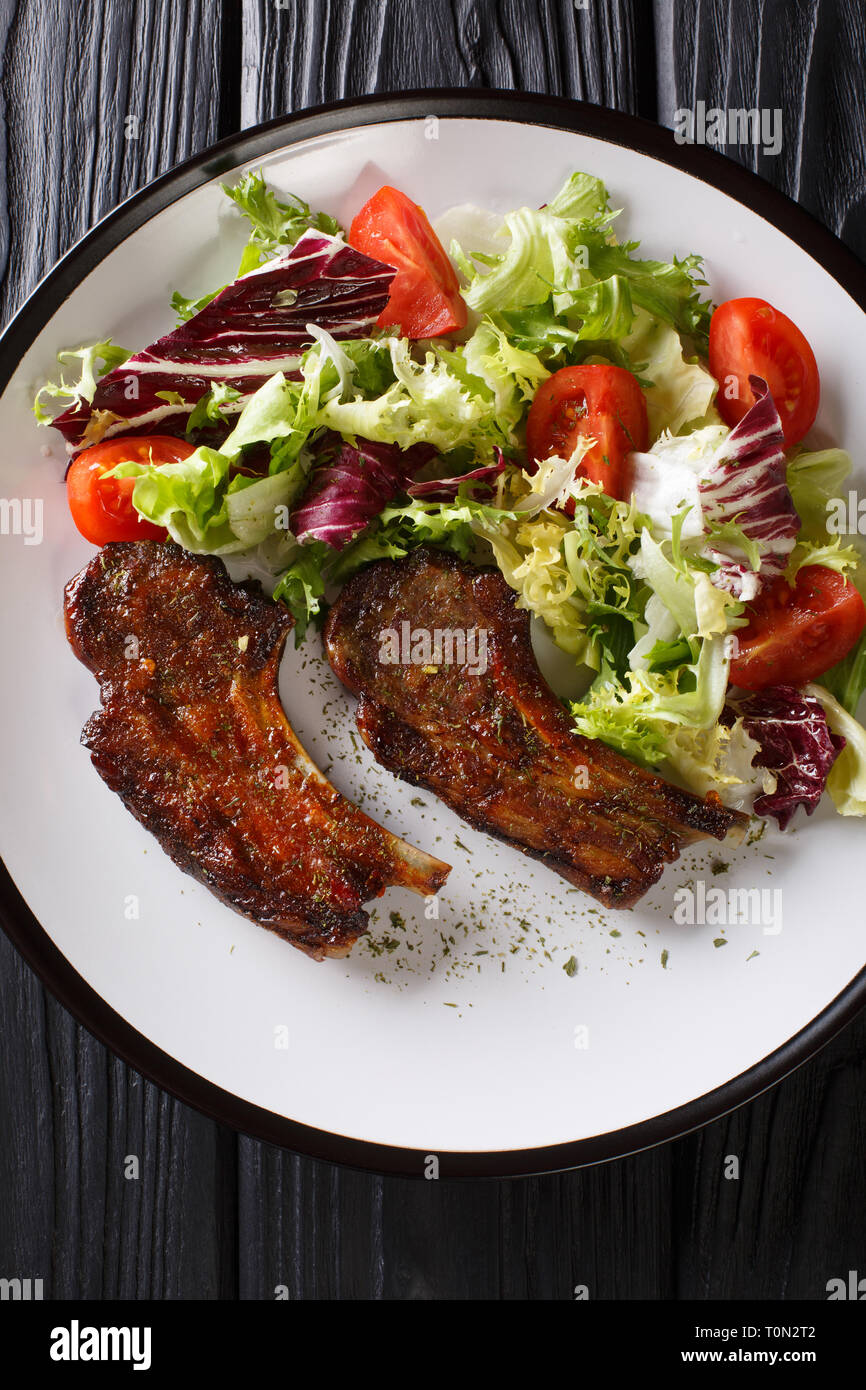 Delicious fried lamb chops served with fresh vegetable salad close-up on a plate on the table. Vertical top view from above Stock Photo