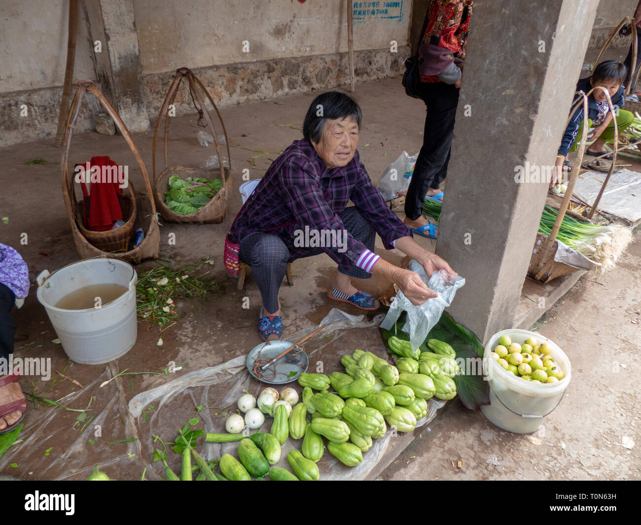 Vendor sells a small selection of fruit and vegetables in the food market of Jianshui, Honghe prefecture, Yunnan province, China. Stock Photo