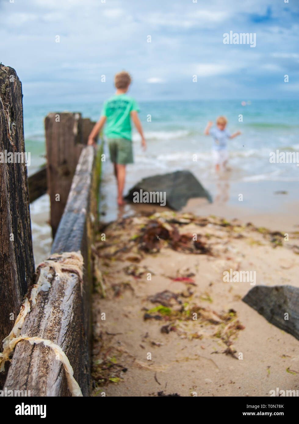 a wooden bar leading into the sea with some kids playing in the sea in summertime Stock Photo