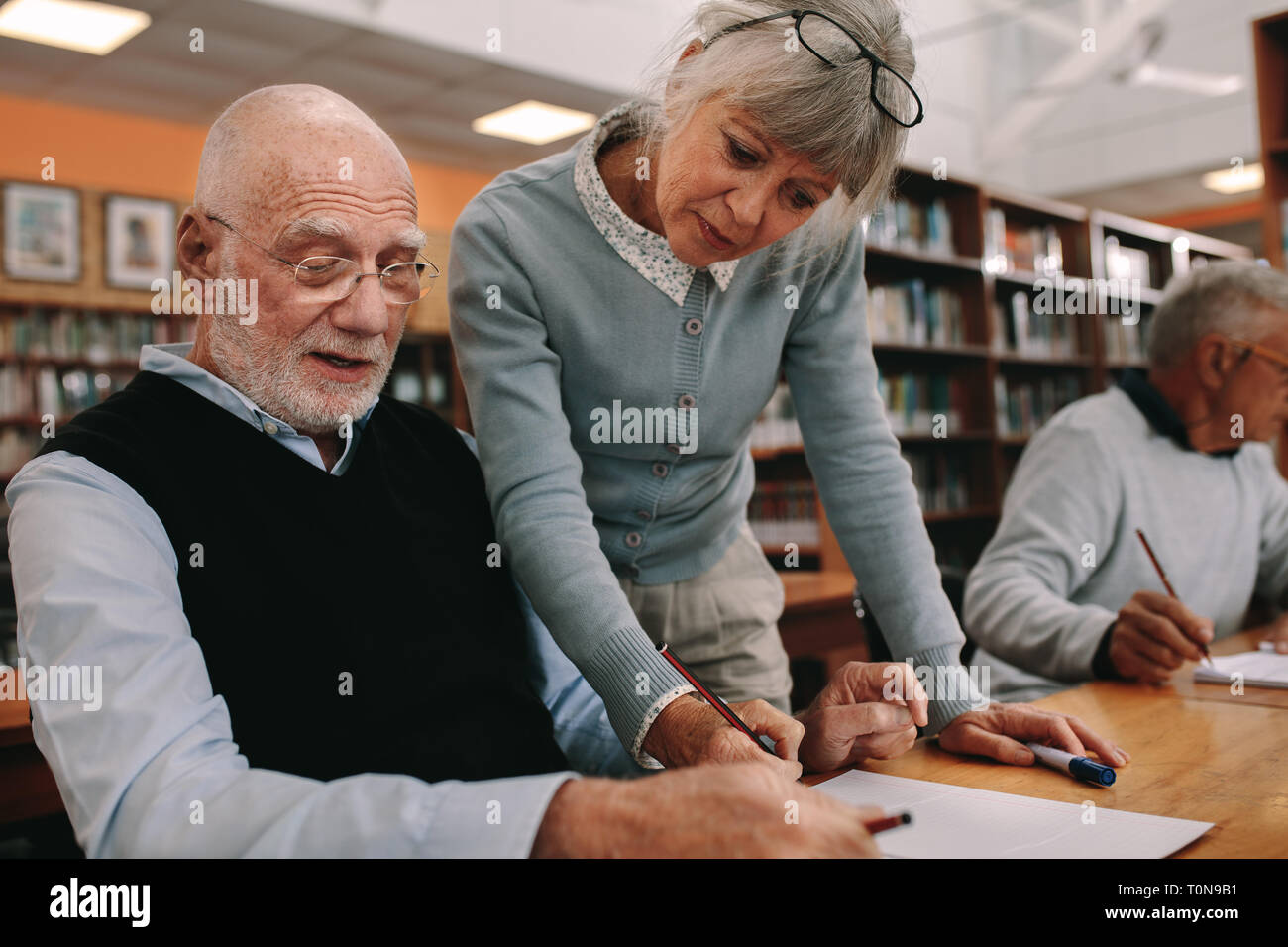 Senior woman lecturer guiding a senior man at college. Senior man sitting in class with his lecturer guiding him in learning. Stock Photo