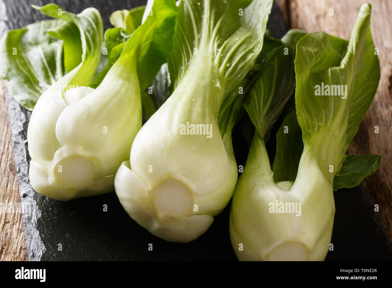 Fresh raw baby bok choy chinese cabbage on a slate board on a wooden table. horizontal Stock Photo