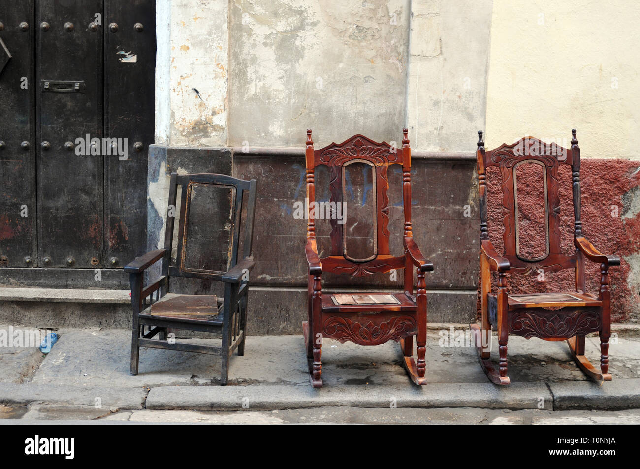 Three wooden chairs sit on a sidewalk in front of a building in Old Havana, Cuba. Stock Photo