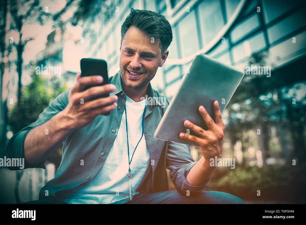 Business executive using mobile phone and digital tablet against office building Stock Photo