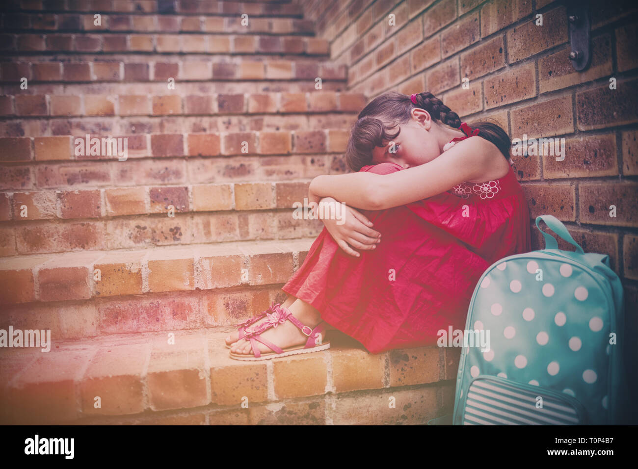 Sad brunette girl seated against a brick wall Stock Photo