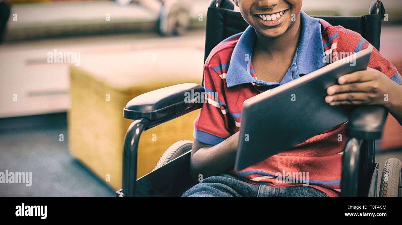 Disabled schoolboy on wheelchair using digital tablet in library Stock Photo