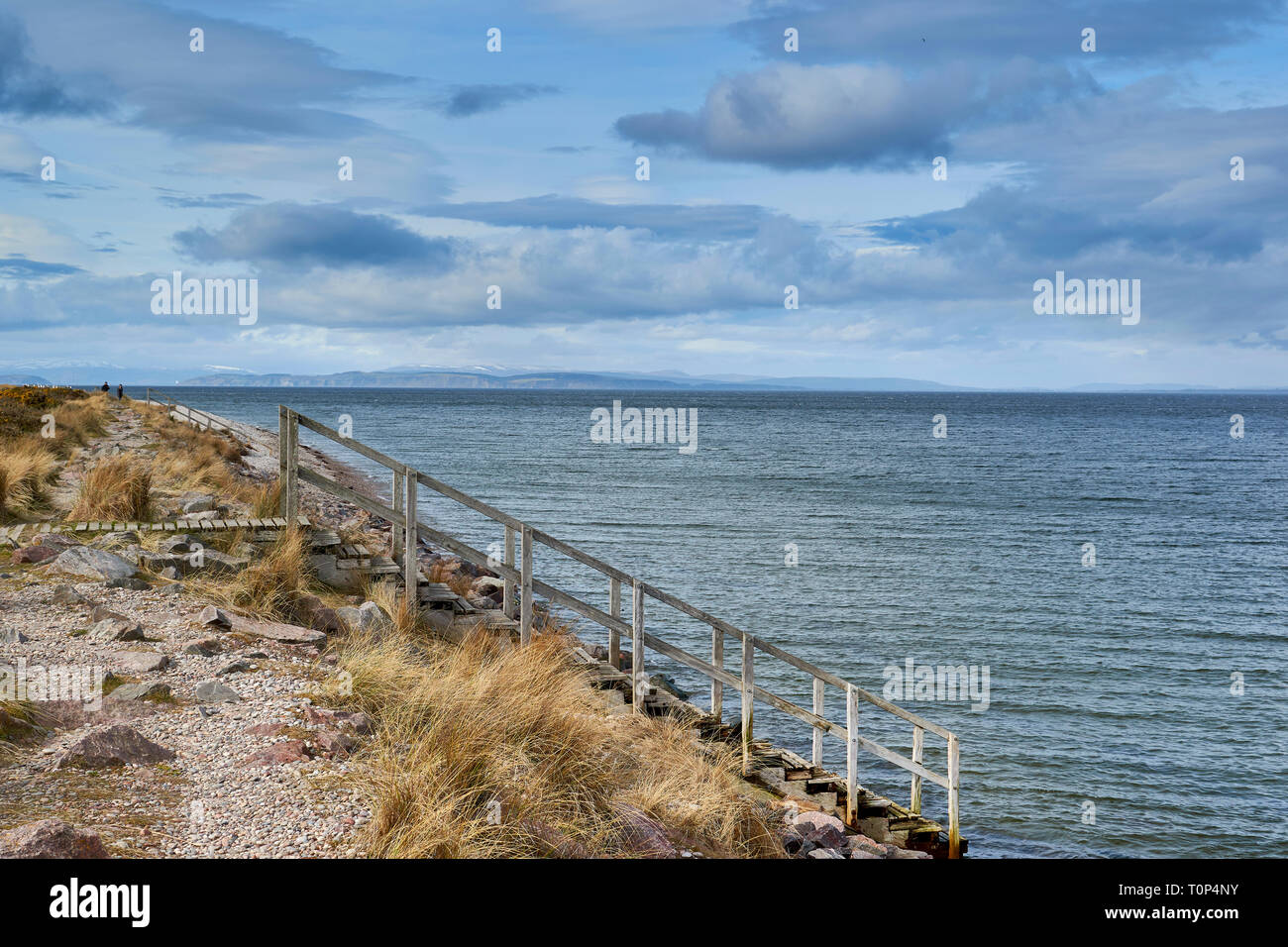 FINDHORN BEACH MORAY FIRTH SCOTLAND WOODEN STEPS LEADING INTO THE SEA THE BLACK ISLE BEYOND AND SNOW ON THE MOUNTAINS Stock Photo