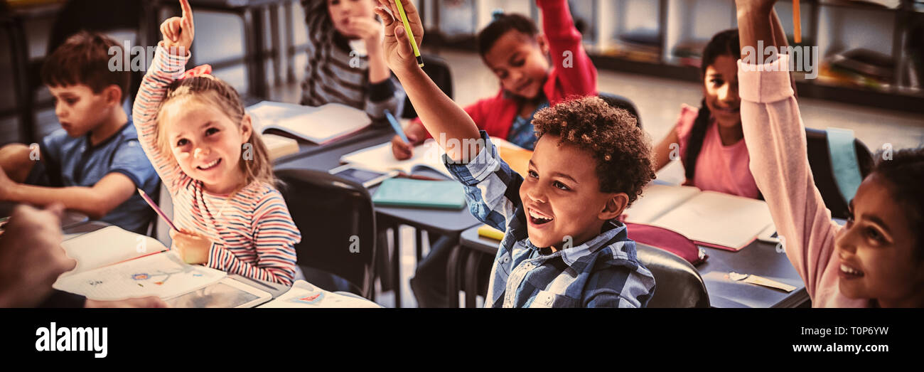 Schoolkids raising their hands in classroom Stock Photo