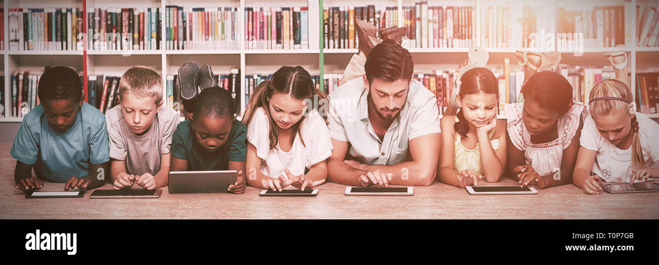 Teacher and kids lying on floor using digital tablet in library Stock Photo