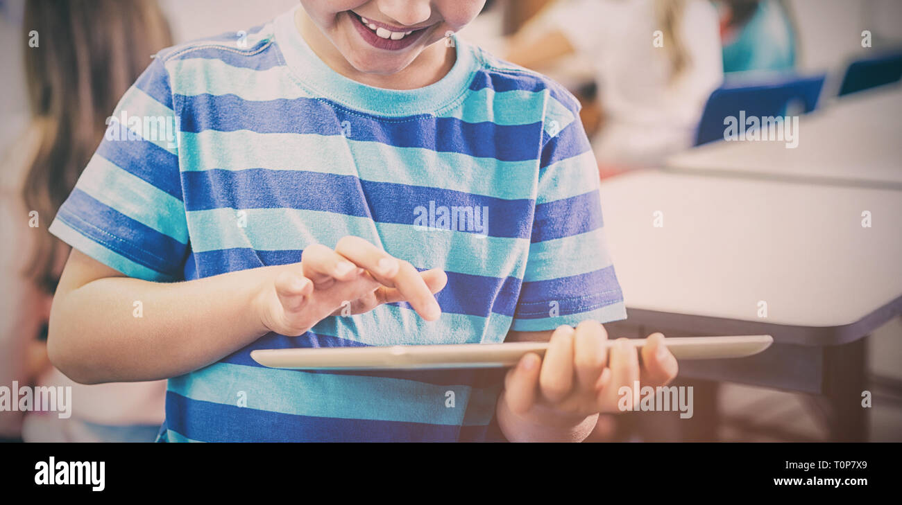 Smiling schoolboy using digital tablet in classroom Stock Photo