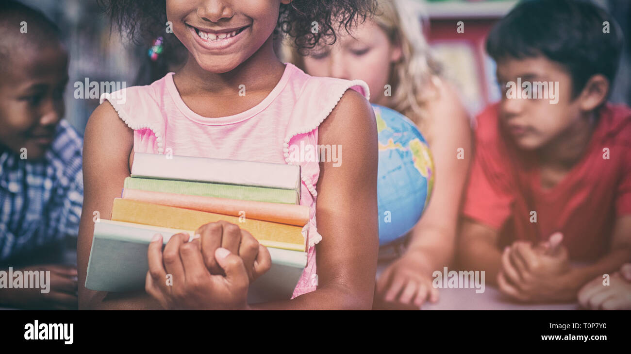 Smiling girl holding books against classmates Stock Photo - Alamy