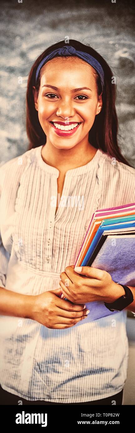 Portrait of smiling school teacher holding books in classroom Stock ...