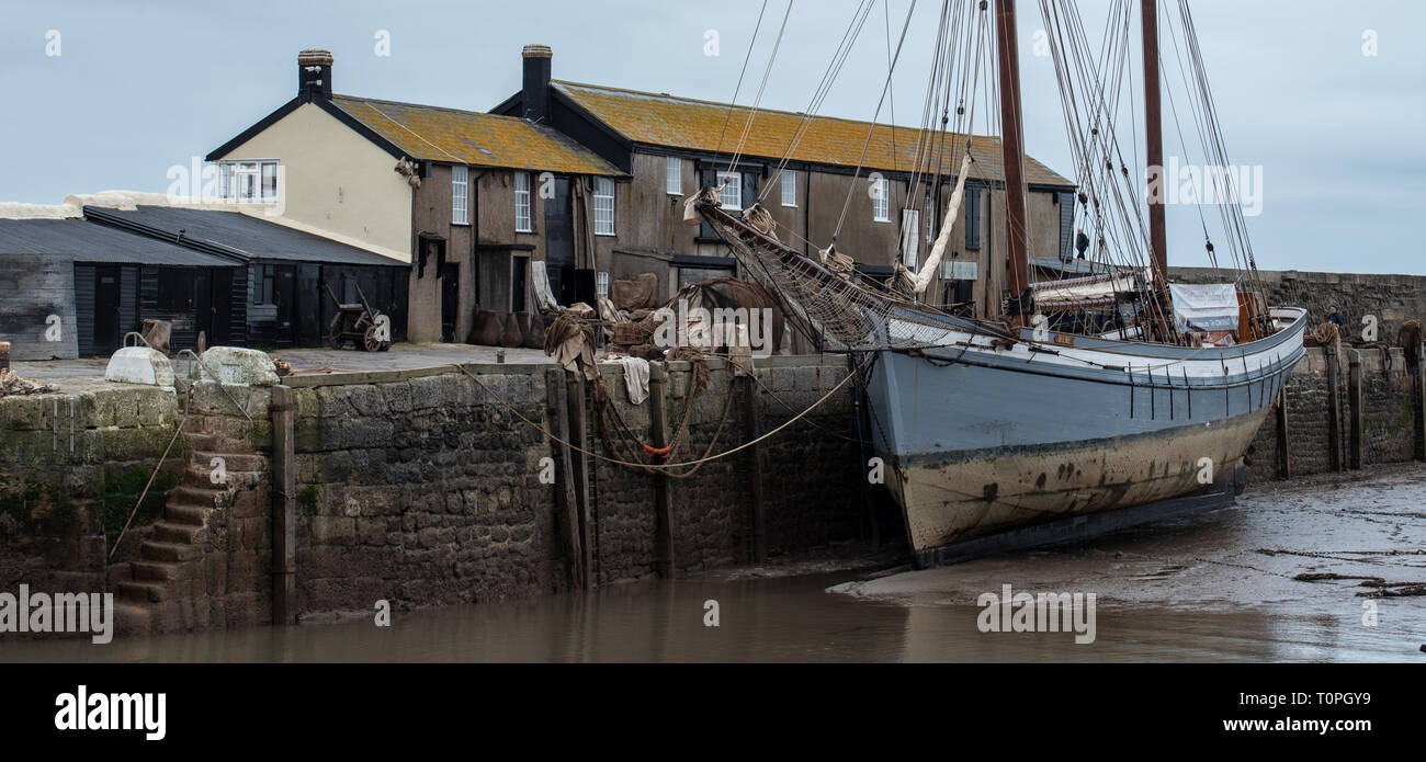 Lyme Regis, Dorset, UK. 21st March 2019. Traditional 1907 sailing Ship 'Irene' moored in Lyme Regis harbour as the 100 foot ketch and the historic Cobb buildings are transformed into a movie set in readiness for continued filming of Ammonite starring Kate Winslet and Saoirse Ronan. Directed by Francis Lee, the fictional drama portrays famous fossil hunter Mary Anning as a gay woman sparking debate among historians and on social media.  The film is expected to bring a welcome boost for tourism and the local economy. Credit: Celia McMahon/Alamy Live News Stock Photo