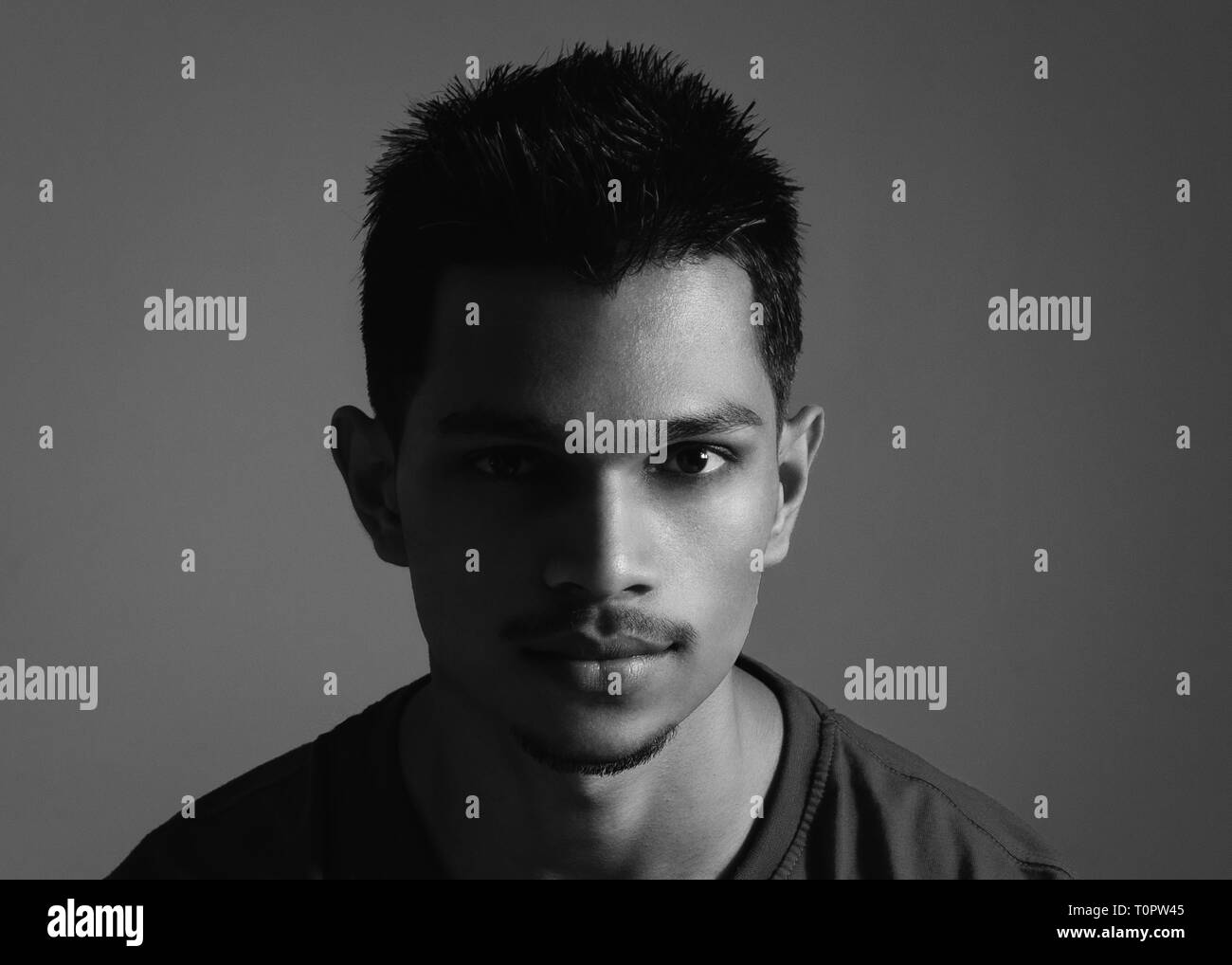 Black and white, headshot, portrait of a 22 years old Indian boy on a plain white background using split lighting. Stock Photo
