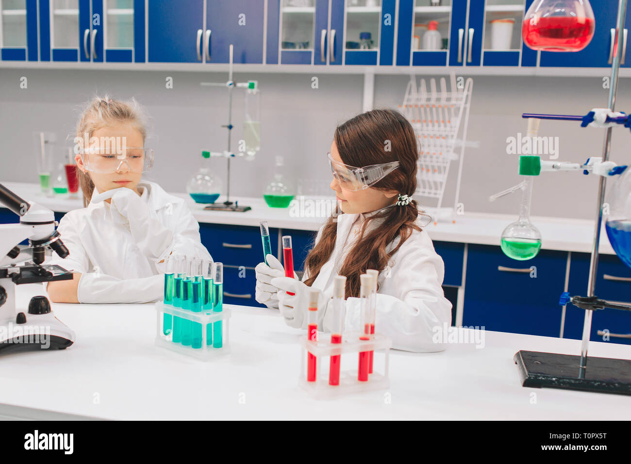Two little kids in lab coat learning chemistry in school laboratory