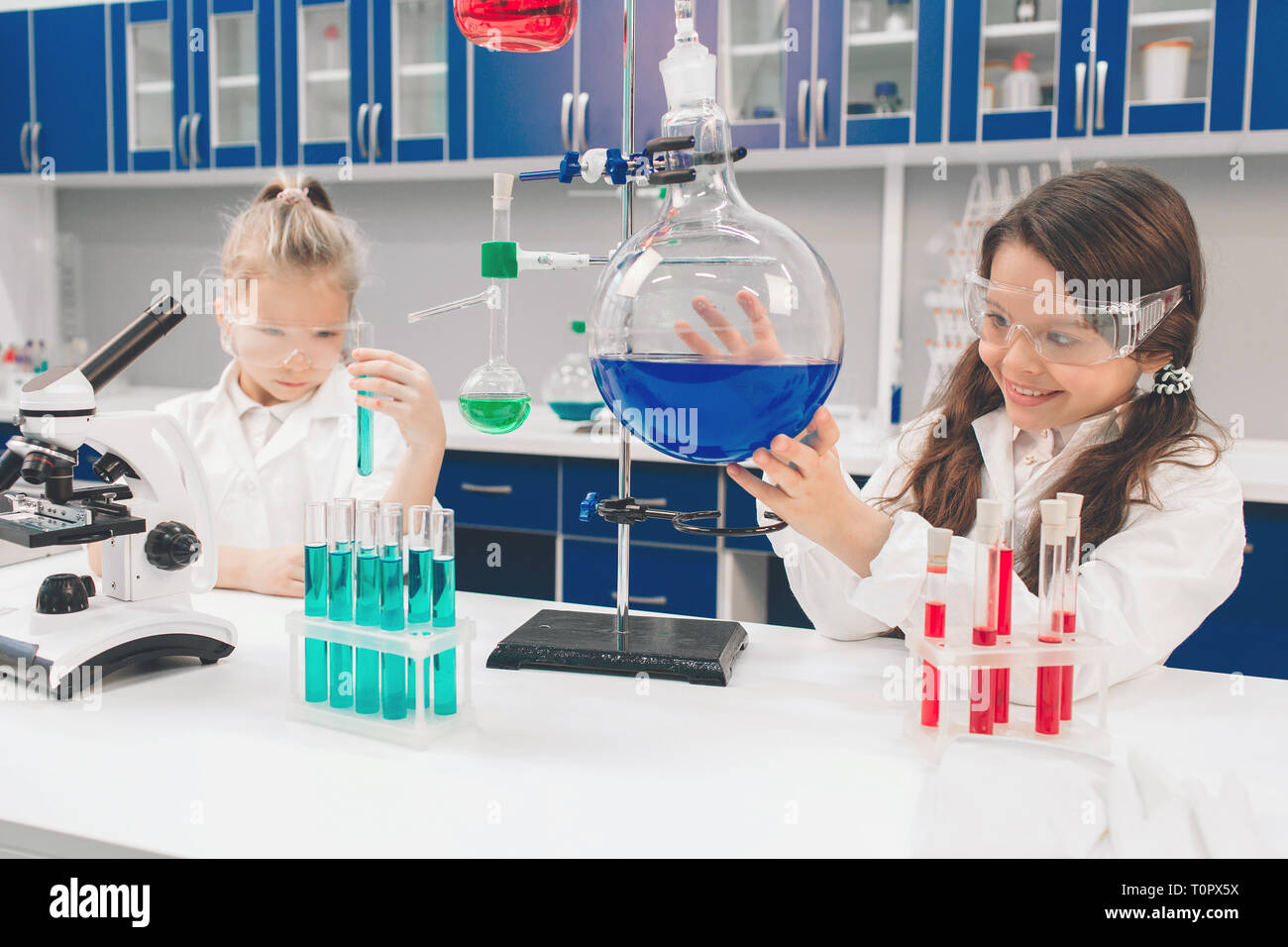 Two little kids in lab coat learning chemistry in school laboratory