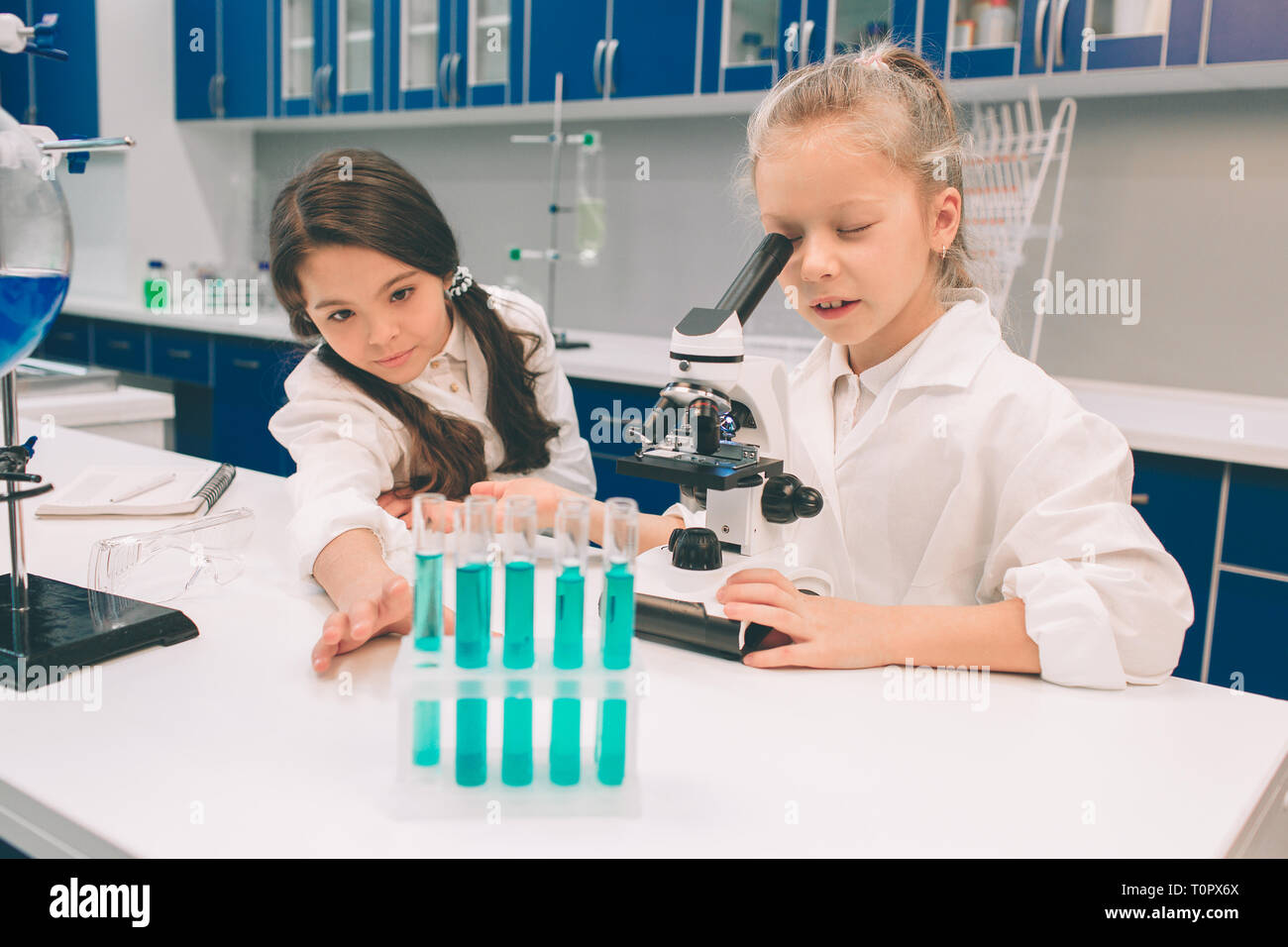 Two little kids in lab coat learning chemistry in school laboratory