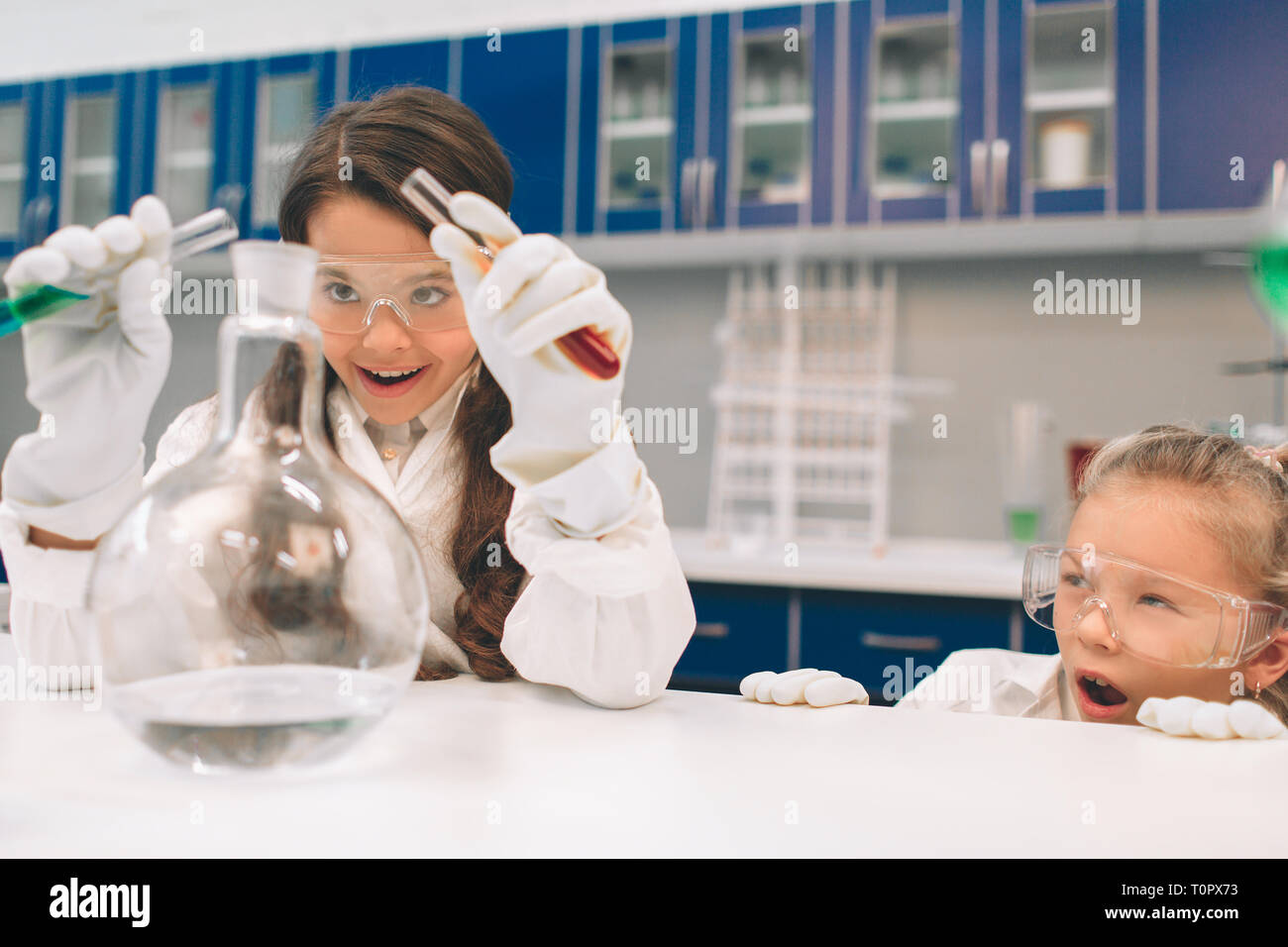 Two little kids in lab coat learning chemistry in school laboratory