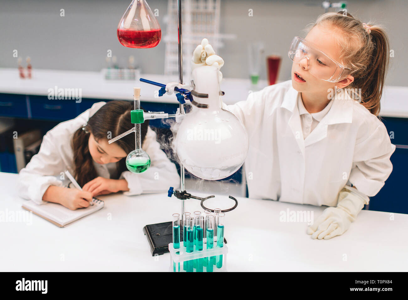 Two little kids in lab coat learning chemistry in school laboratory